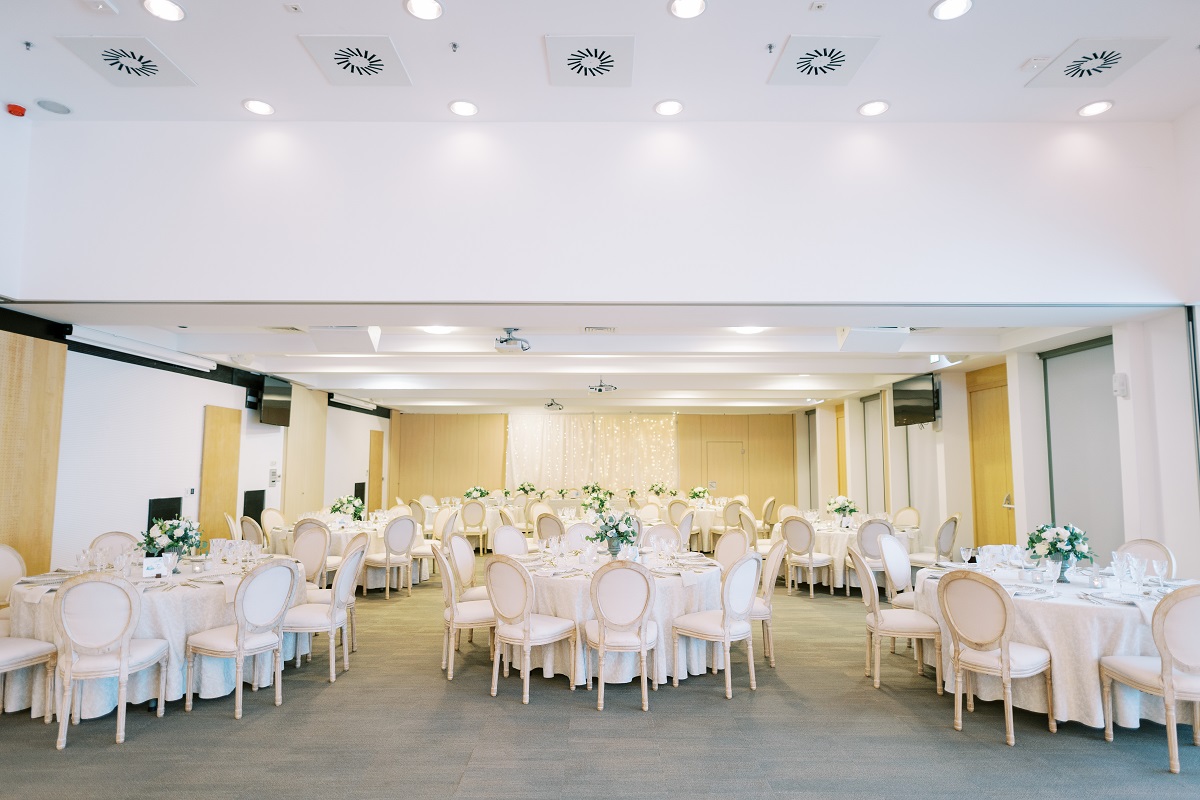 Round festive tables with bouquets surrounded by chairs in an illuminated banquet hall